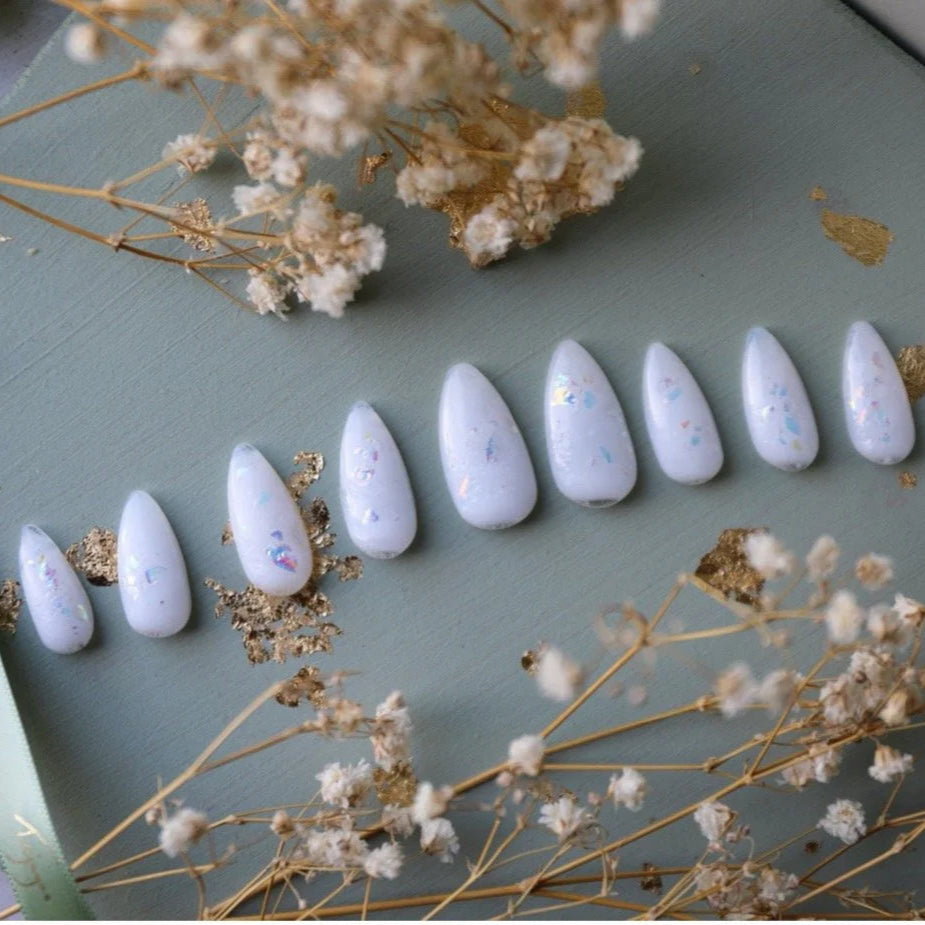 Set of white nail polish samples on a green surface with dried flowers.